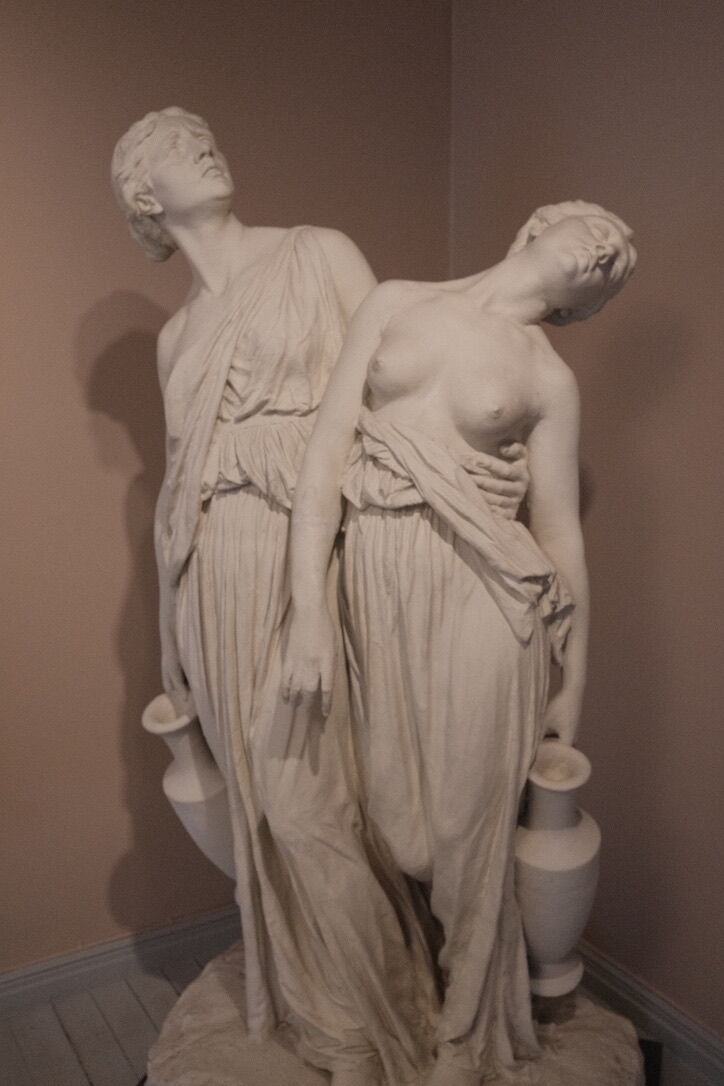 A marble sculpture depicting two women in flowing dresses, one leaning back and the other holding a vase.